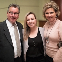 A graduate student posing for a photo with her parents at the reception